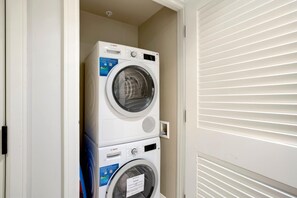 A stacked washer and dryer unit in a laundry room with a door and blinds. - Honua Kai 4 Free Cars KBM Resorts Front Alii Suite 4 Units, 8 Bedrooms HK Ml-3182 (Kaanapali)