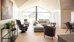 Un saló modern amb un sofà modular, dues butaques reclinables, una taula de centre i una zona de menjador amb cadires.