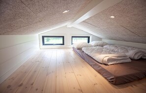 A bedroom with a sloped ceiling, wooden flooring, a bed with white bedding, and two windows. - Pet friendly home in Sæby with sauna (Sæby)
