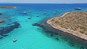 A coastal area with boats, clear turquoise water, rocky terrain, and a small island. - Sun-Kissed Sailing Adventure in the Stunning Islas Cícladas (Paros)