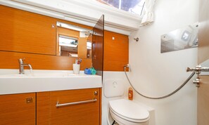 A compact bathroom with a wooden vanity, a toilet, and a shower. - Sun-Kissed Sailing Adventure in the Stunning Islas Cícladas (Paros)