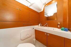A bathroom with wooden cabinets, a white sink, a mirror, and a toilet. - Sun-Kissed Sailing Adventure in the Stunning Islas Cícladas (Paros)