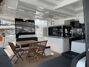 A boat's interior with a dining area, seating, and a small kitchen.