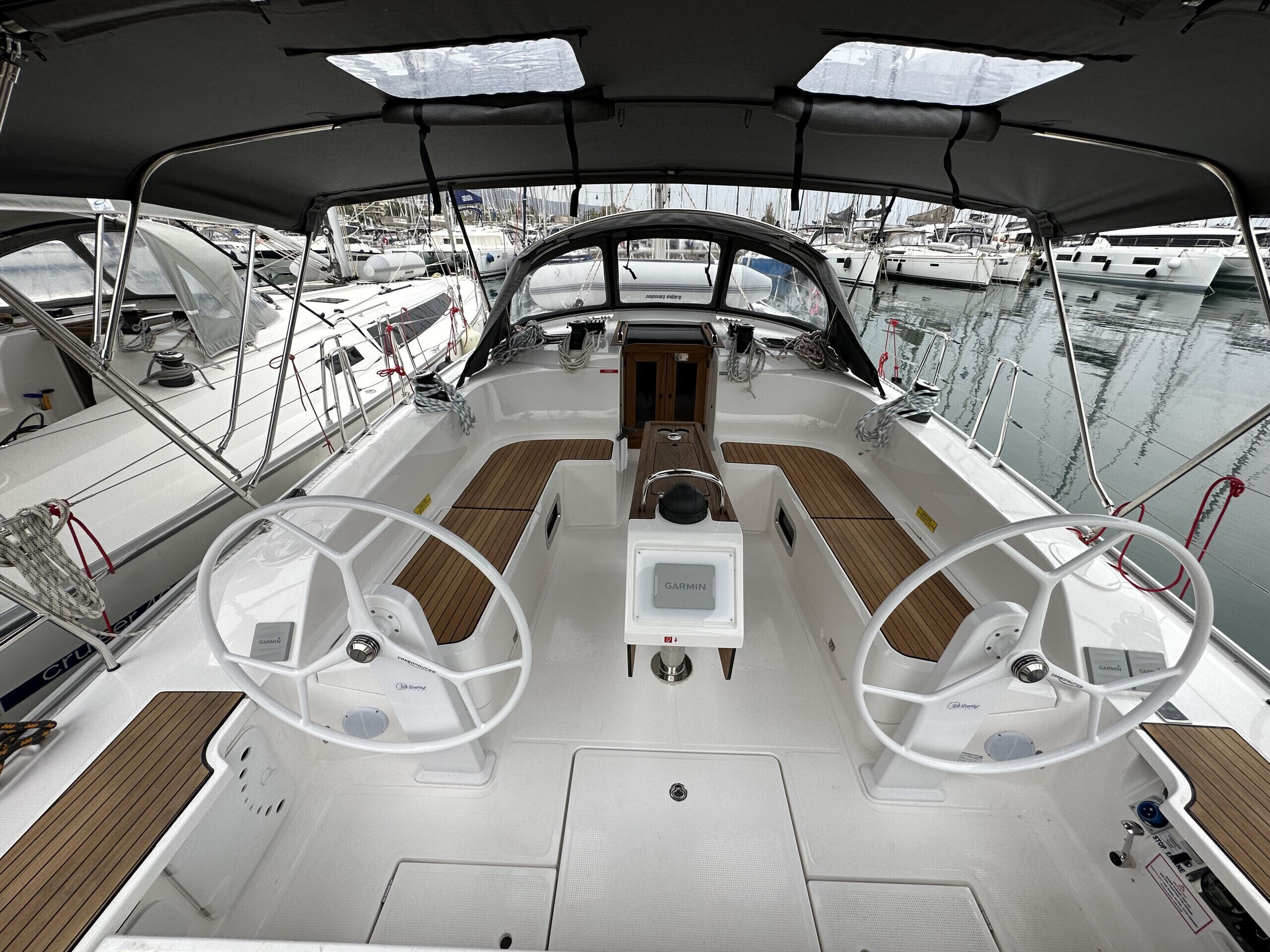 A boat deck with two steering wheels, a central table, and a view of other boats in the marina.