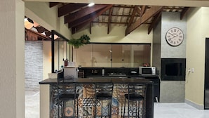 A kitchen with a bar area, a clock, and a stone wall. - LUXURIOUS HOUSE IN MARINAS DI CALDAS CONDOMINIUM (caldas novas)
