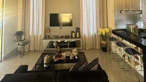 A modern living room with a sofa, coffee table, TV, and kitchen area with bar stools. - LUXURIOUS HOUSE IN MARINAS DI CALDAS CONDOMINIUM (caldas novas)