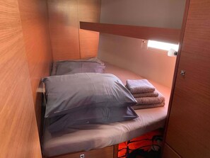 A compact bed with pillows and a folded blanket, a wooden headboard, and a small overhead light. - Sun-Kissed Sailing Adventure in the Saronic Islands (Laurium)