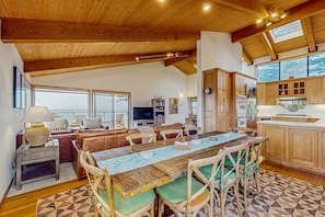A spacious living area with a large wooden dining table, comfortable seating, and a kitchen with wooden cabinets. - Oceanfront home with hot tub & garden near the bluffs, dogs welcome (Sea Ranch)