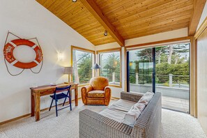 A room with a wooden ceiling, a desk with a chair, a sofa, and large windows offering a view of trees. - Oceanfront home with hot tub & garden near the bluffs, dogs welcome (Sea Ranch)