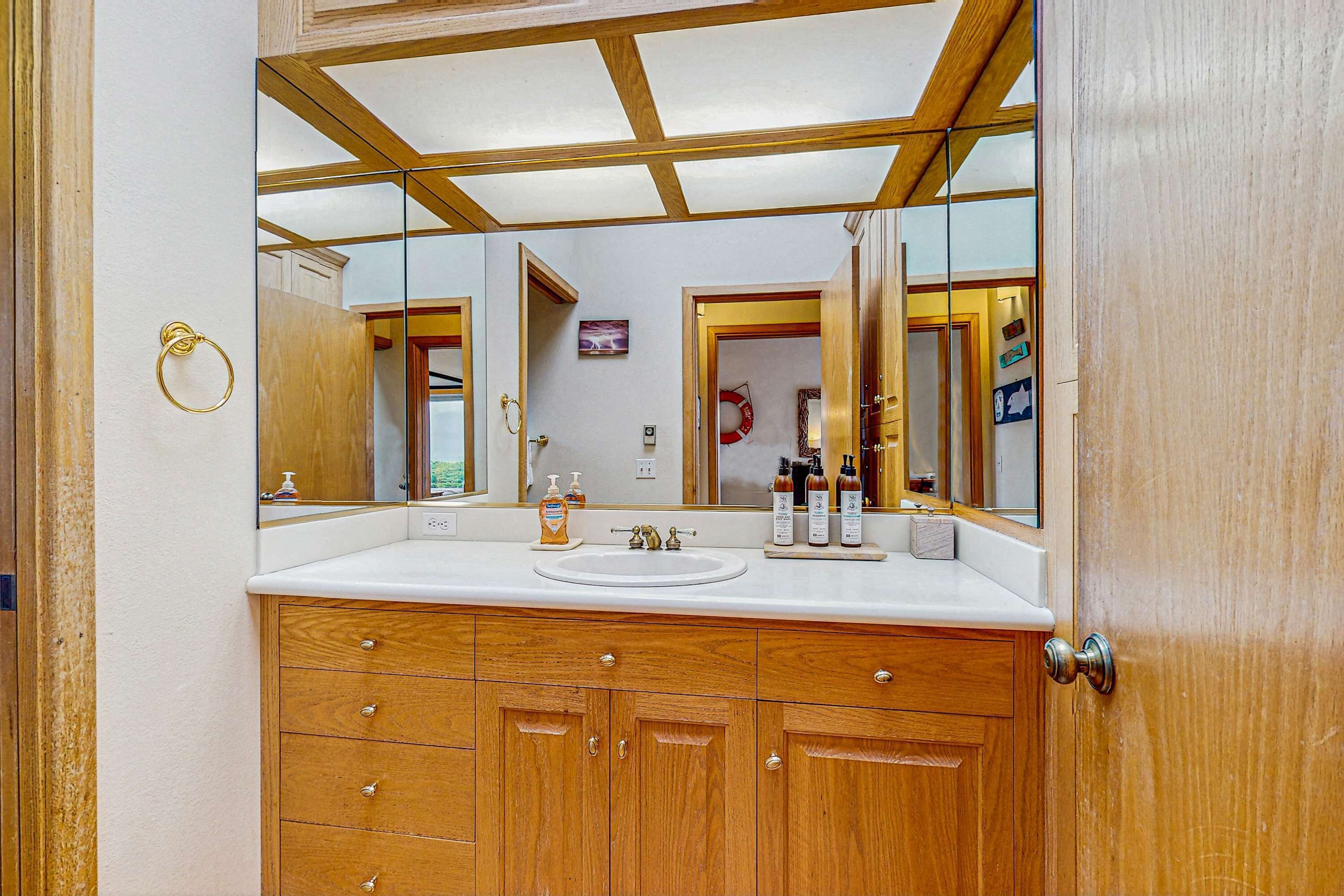 A bathroom with a large mirror, wooden cabinets, a sink, and toiletries.