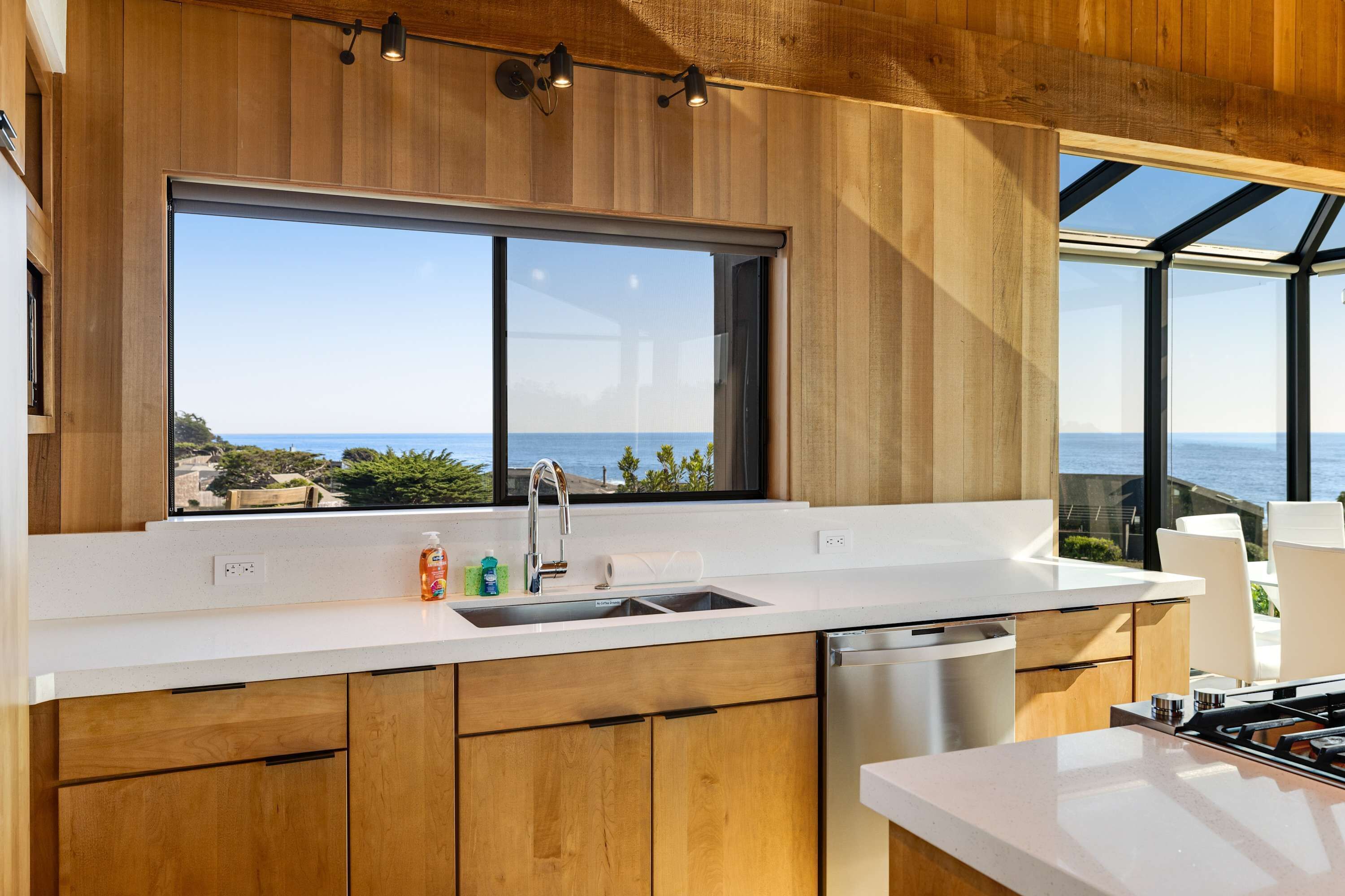 Eine moderne Küche mit Holzausstattung, einer Edelstahlspüle und einem großen Fenster mit Meerblick.