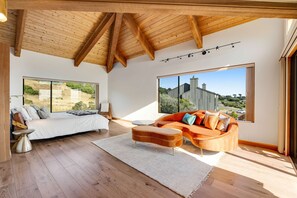 Een moderne woonkamer met een bed, een oranje bank en grote ramen.