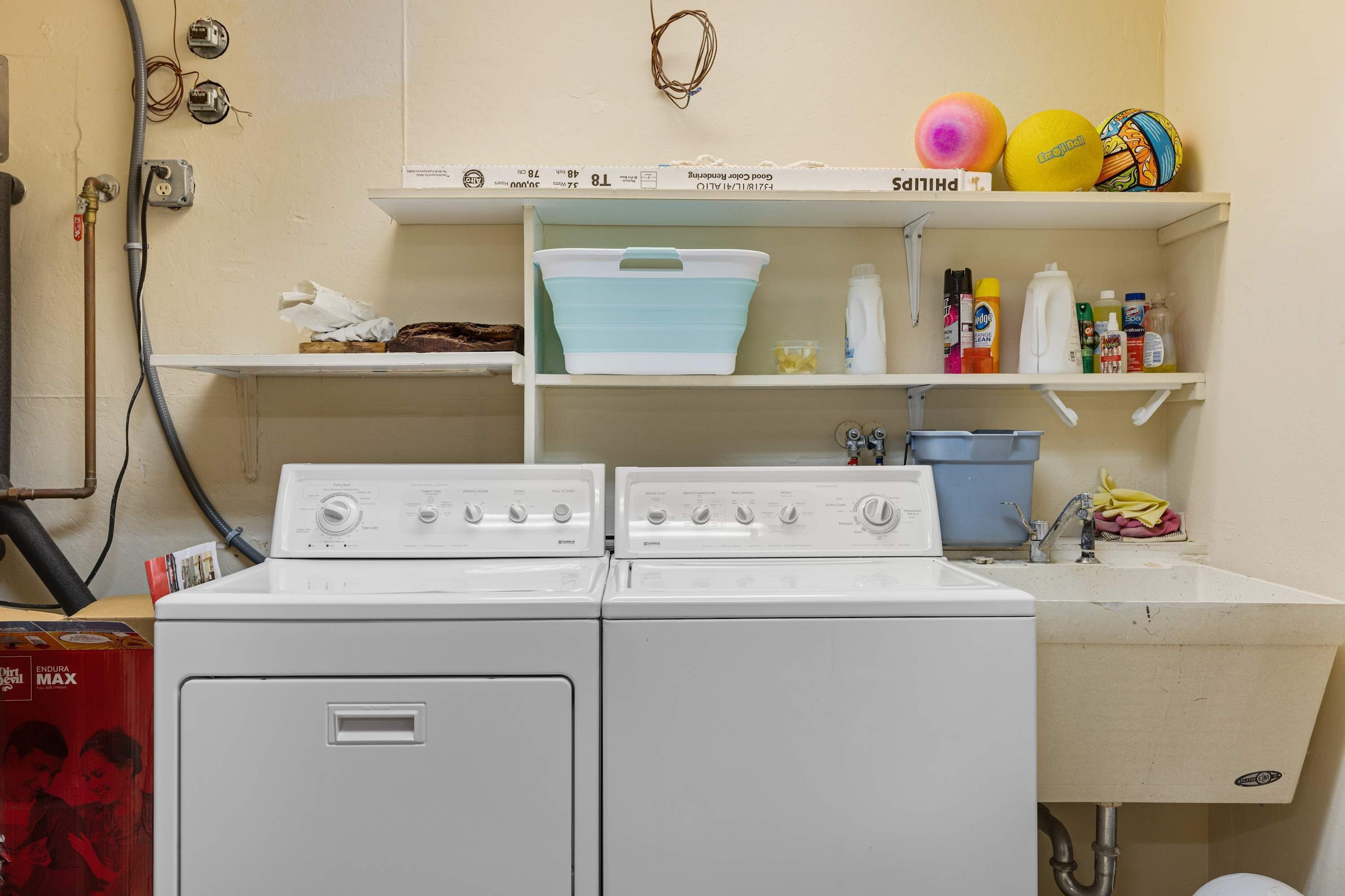 A laundry room with two washing machines, a sink, and shelves with various items.
