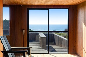 Ein Holzinnenraum mit einer großen Schiebeglasdoor, die auf eine Terrasse mit Meerblick führt.