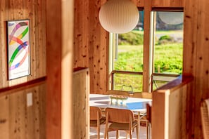 Ein Holzinstrument mit einem Esstisch, Stühlen, einer Hängelampe und einem Fenster mit Blick auf Grünflächen.