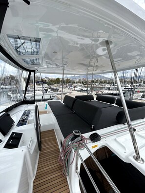 A boat deck with seating, a steering wheel, and a view of the marina. - Sun-Kissed Sailing Adventure in Islas Esporadas (Skiathos)