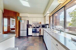 A modern kitchen with a large window, stainless steel appliances, and a view of the outdoors. - Oceanfront home with private hot tub near Shell Beach (Sea Ranch)