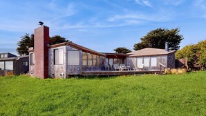 A modern house with a brick chimney, large windows, and a covered patio area. - Sea Ranch 4BR oceanfront home with private hot tub near Shell Beach (Sea Ranch)