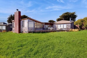 A modern house with a brick chimney, large windows, and a covered patio area. - Oceanfront home with private hot tub near Shell Beach (Sea Ranch)
