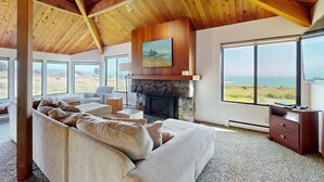 A spacious living room with a stone fireplace, large windows, and a high wooden ceiling. - Sea Ranch 4BR oceanfront home with private hot tub near Shell Beach (Sea Ranch)