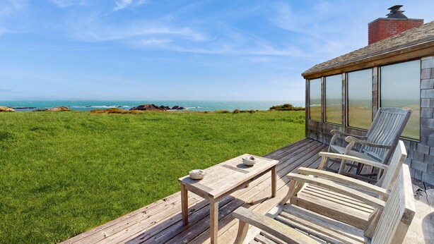 A wooden deck with a table and chairs, overlooking a grassy field and the ocean. - Sea Ranch 4BR oceanfront home with private hot tub near Shell Beach (Sea Ranch)