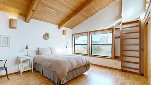 Ein Schlafzimmer mit Bett, Nachttisch, Lampe, Sessel und einem Fenster mit Blick.