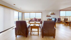 Ein geräumiger Wohnbereich mit großem Fenster zum Strand, Ledersofas, einem Holztisch und einem kleinen Beistelltisch.