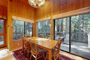 Un intérieur en bois avec une table et des chaises, de grandes fenêtres et une vue sur la forêt.