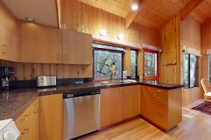 Une cuisine rustique, située dans une cabane en bois, équipée d’un lave-vaisselle, d’un grille-pain et d’une fenêtre donnant sur la forêt.