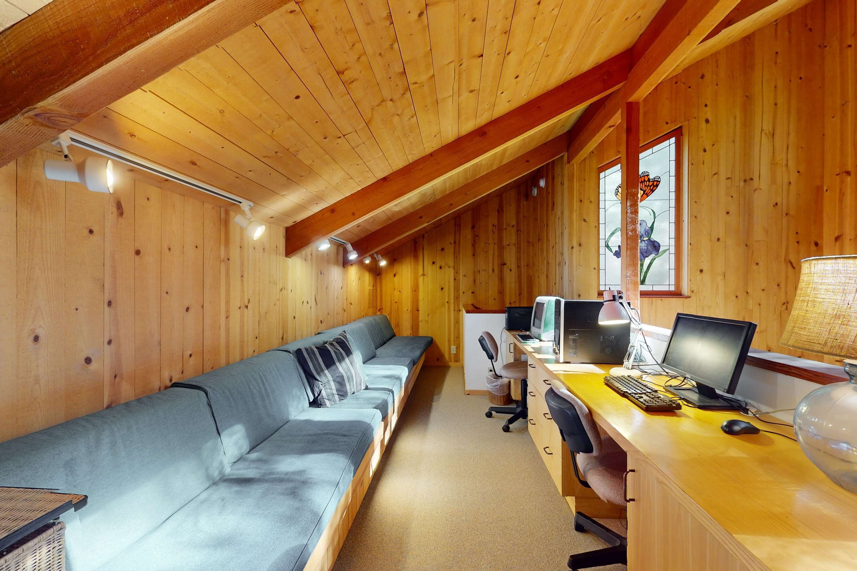 Une cabane en bois avec un long canapé, un bureau avec un ordinateur et une lampe.