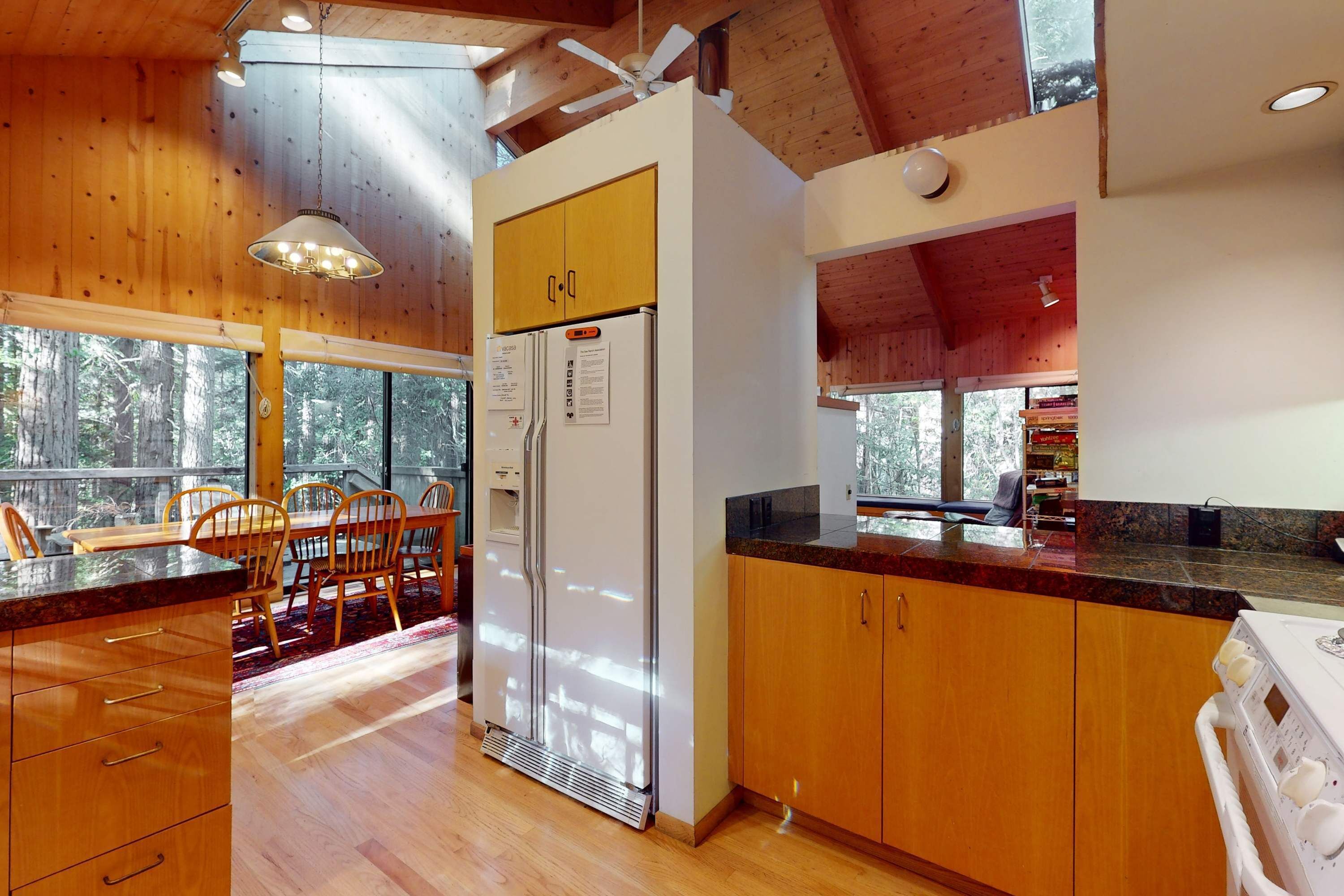 A modern kitchen with wooden cabinets, a built-in refrigerator, and a dining area with wooden chairs and a table.