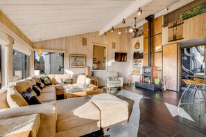 A spacious living area with a wooden ceiling, a large sofa, a coffee table, and a bar area with stools. - Esherick-designed home with private hot tub near Black Point, dogs welcome (Sea Ranch)
