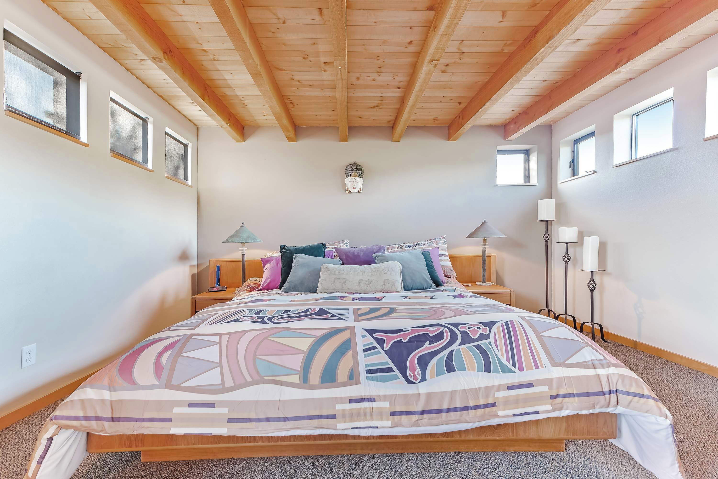 A bedroom with a wooden ceiling, a bed with patterned bedding, bedside lamps, and a wall-mounted light fixture.