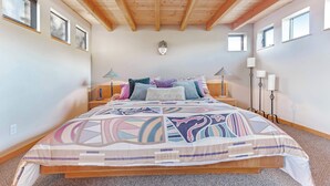 Une chambre avec un plafond en bois, un lit avec une literie à motifs, des lampes de chevet et un luminaire fixé au mur.
