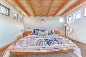 A bedroom with a wooden ceiling, a bed with patterned bedding, bedside lamps, and a wall-mounted light fixture. - Sea Ranch 1BR meadow cottage with hot tub near Del Mar pool (Sea Ranch)