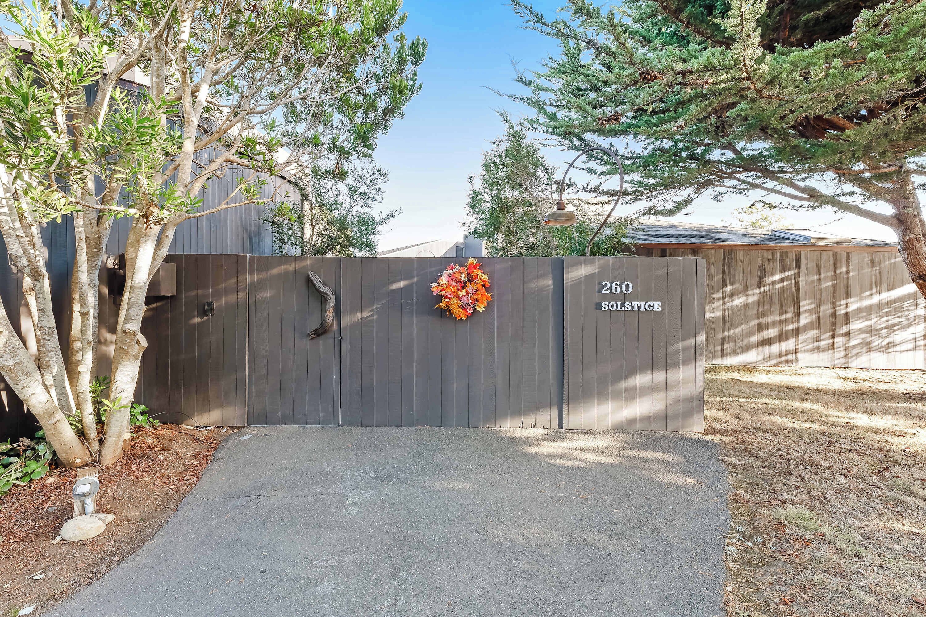A gated entrance with a wooden fence, a number sign '260 Solstice,' and a flower arrangement.