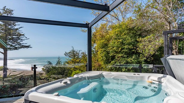 A hot tub with a clear view of the ocean and surrounding greenery. - Updated home with ocean views, private hot tub, fire table, outdoor kitchen (Gualala)