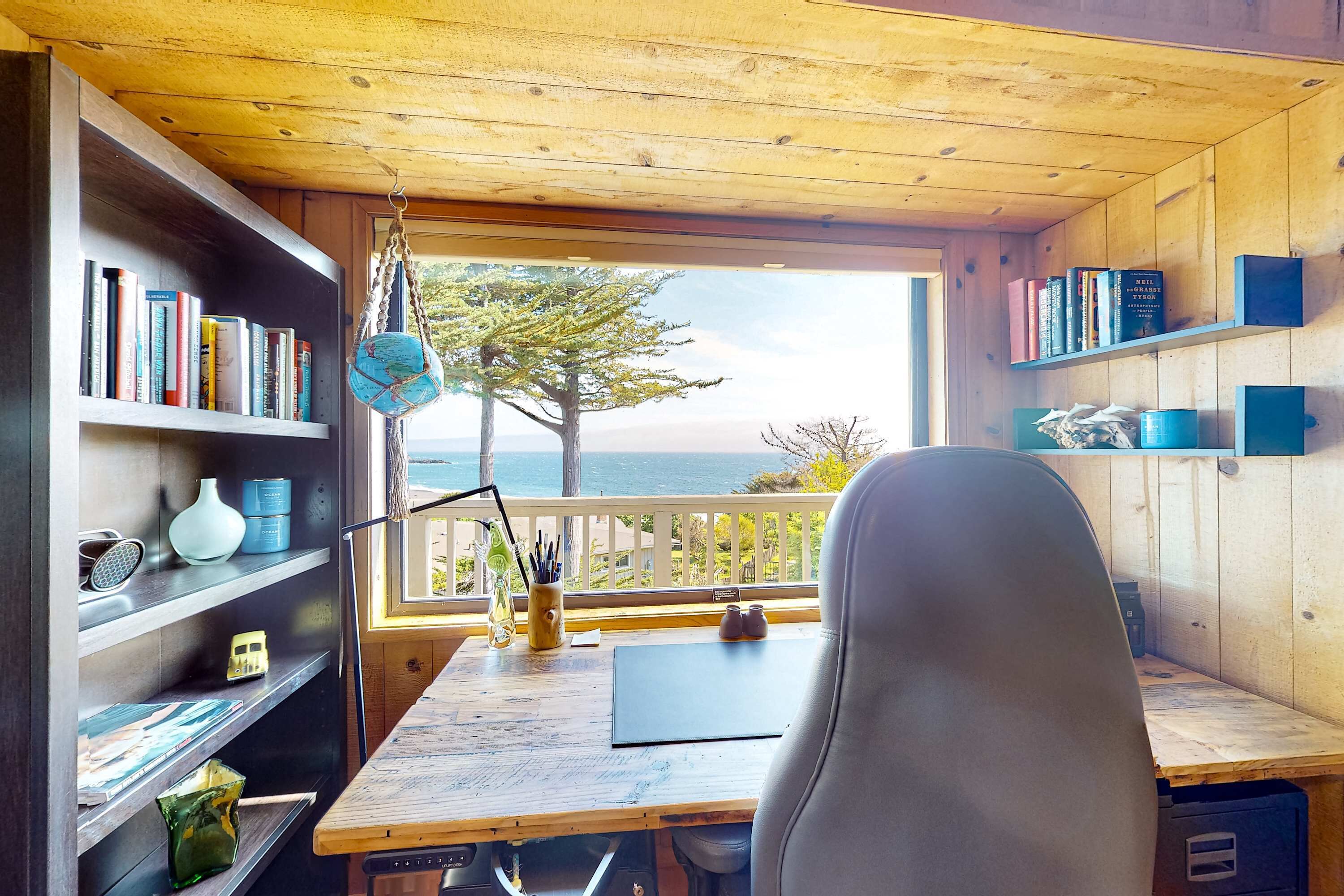 Una cabaña de madera con escritorio, estanterías y vista al océano.