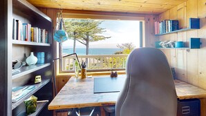 A wooden cabin with a desk, bookshelves, and a view of the ocean. - Updated home with ocean views, private hot tub, fire table, outdoor kitchen (Gualala)