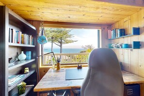 Eine Holzhütte mit Schreibtisch, Bücherregalen und Blick auf den Ozean.