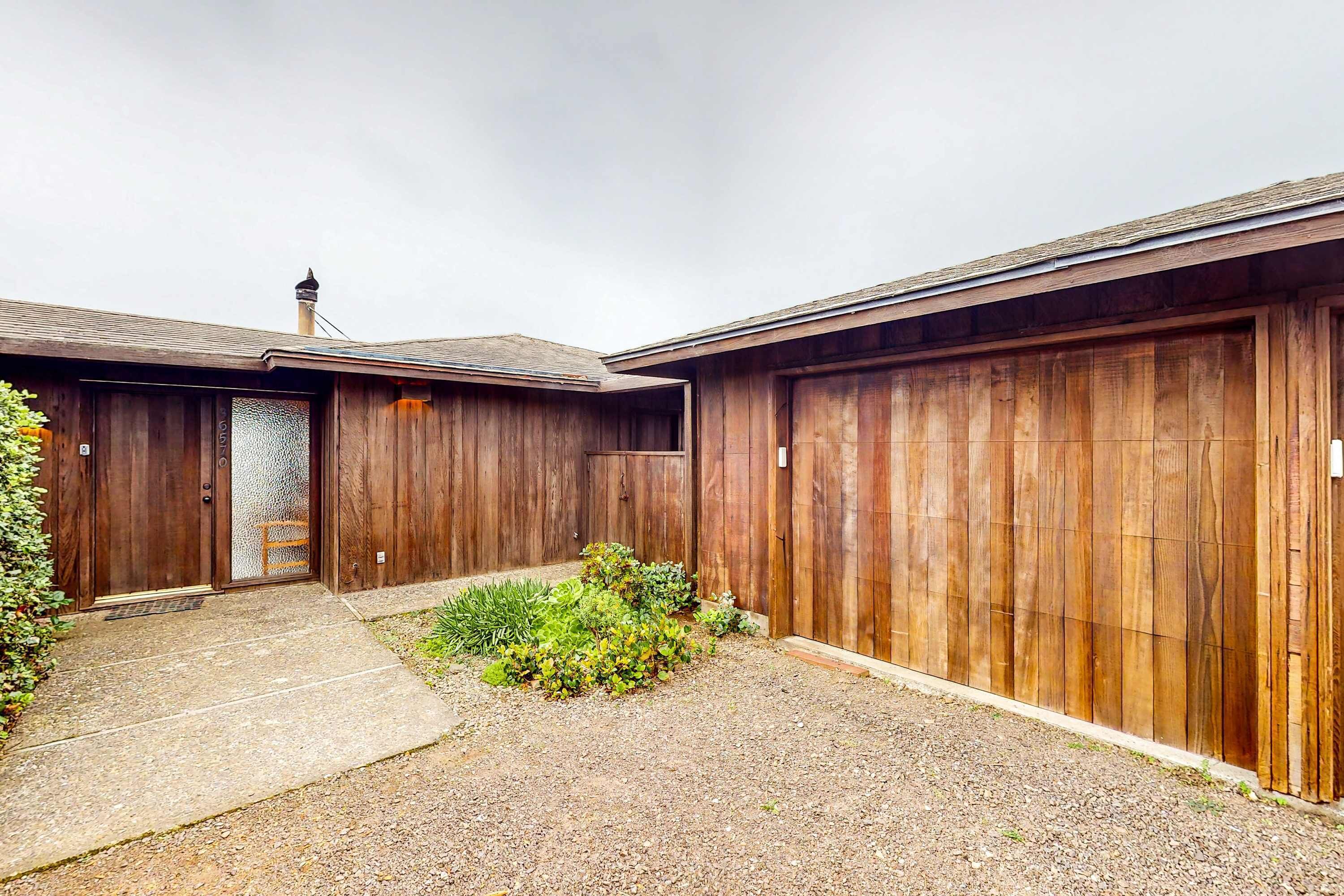 A wooden building with a garage door, a concrete pathway, and some greenery.