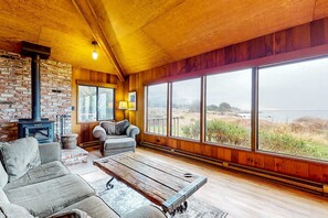 Ein gemütliches Zimmer mit Kamin, großen Fenstern und Blick ins Grüne.