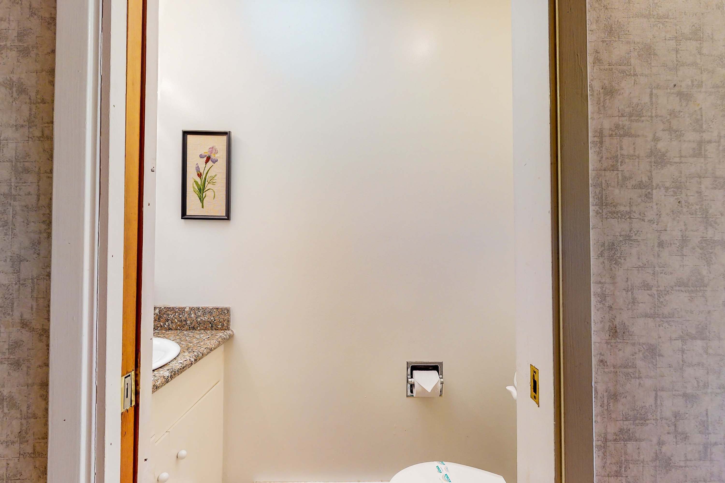Une salle de bain avec un lavabo blanc, une œuvre d’art florale encadrée et un porte-rouleau de papier toilette.