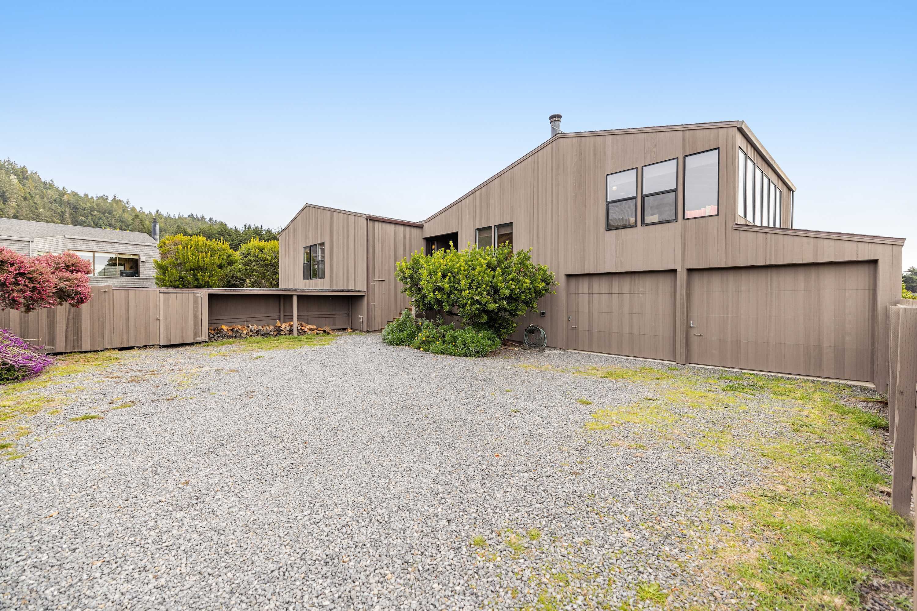 A modern building with a gravel driveway, a wooden fence, and a small tree.