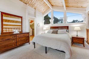 Une chambre à coucher avec une tête de lit en bois, un grand lit, une commode et une fenêtre avec des rideaux.