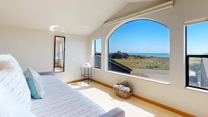 A bedroom with a large window, a bed, a small table, and a basket. - Sea Ranch 2BR modern ocean-view home on golf course with hot tub (Sea Ranch)