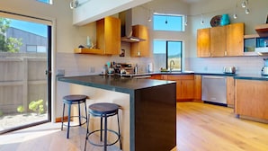 A modern kitchen with a large island, wooden cabinets, and a view through a sliding door. - Sea Ranch 2BR modern ocean-view home on golf course with hot tub (Sea Ranch)