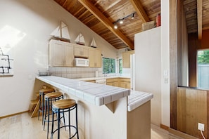 A kitchen with wooden beams, a white countertop, and wooden stools. - Meadow home with private hot tub near Black Point Beach (Sea Ranch)
