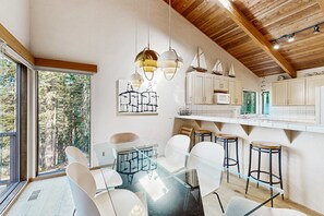 A modern kitchen with white cabinets, a glass dining table, and hanging pendant lights. - Meadow home with private hot tub near Black Point Beach (Sea Ranch)
