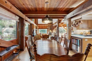 A wooden dining table with chairs, a hanging light fixture, and a view of the outdoors. - Sea Ranch 2BR Binker Barn with hot tub, yard & fire pit — dogs welcome (Sea Ranch)